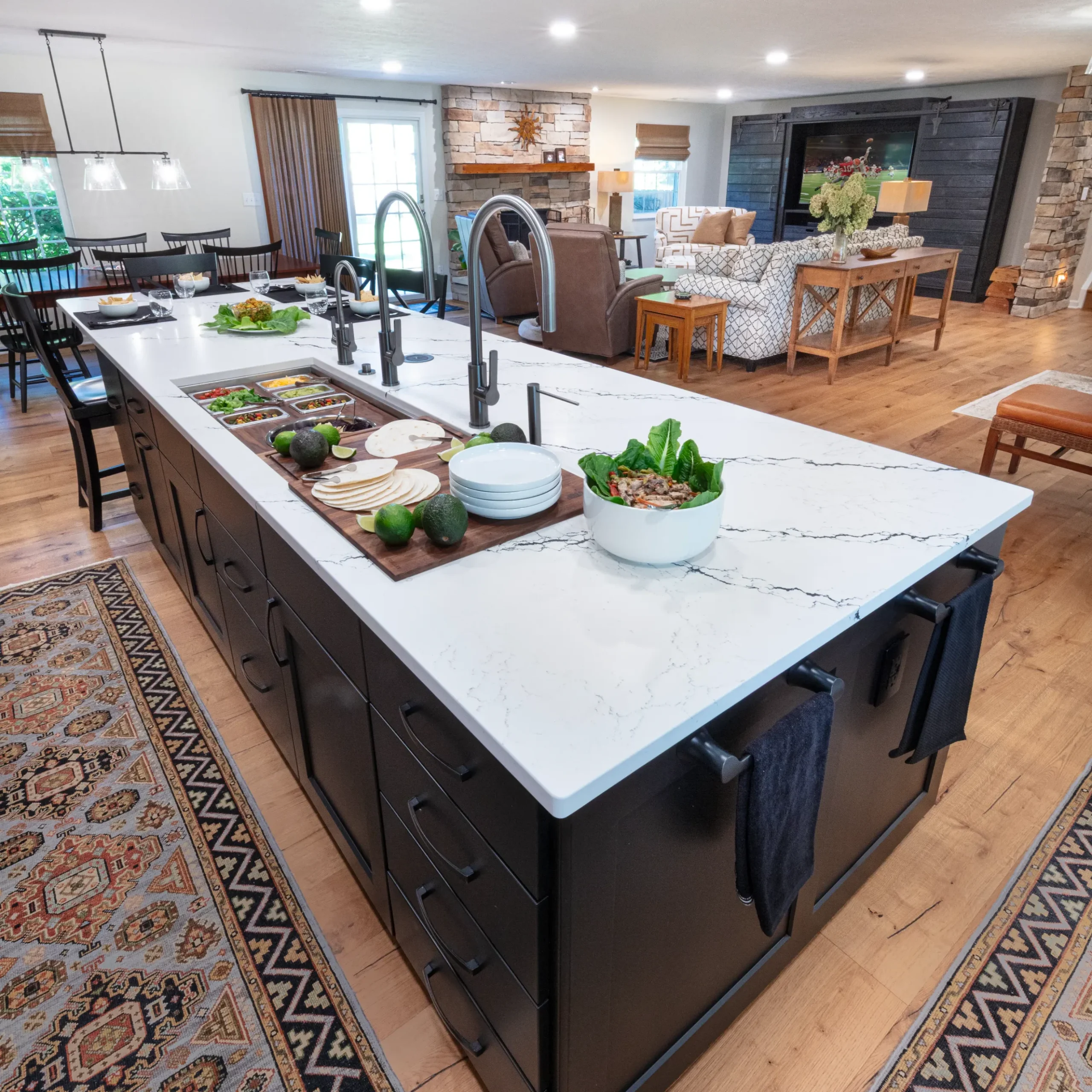 Large kitchen island with quartz countertops overlooking an open living room with a stone fireplace.