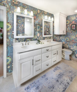 Bright bathroom with bold floral wallpaper, a white double-sink vanity, illuminated mirrors, and brushed nickel fixtures.