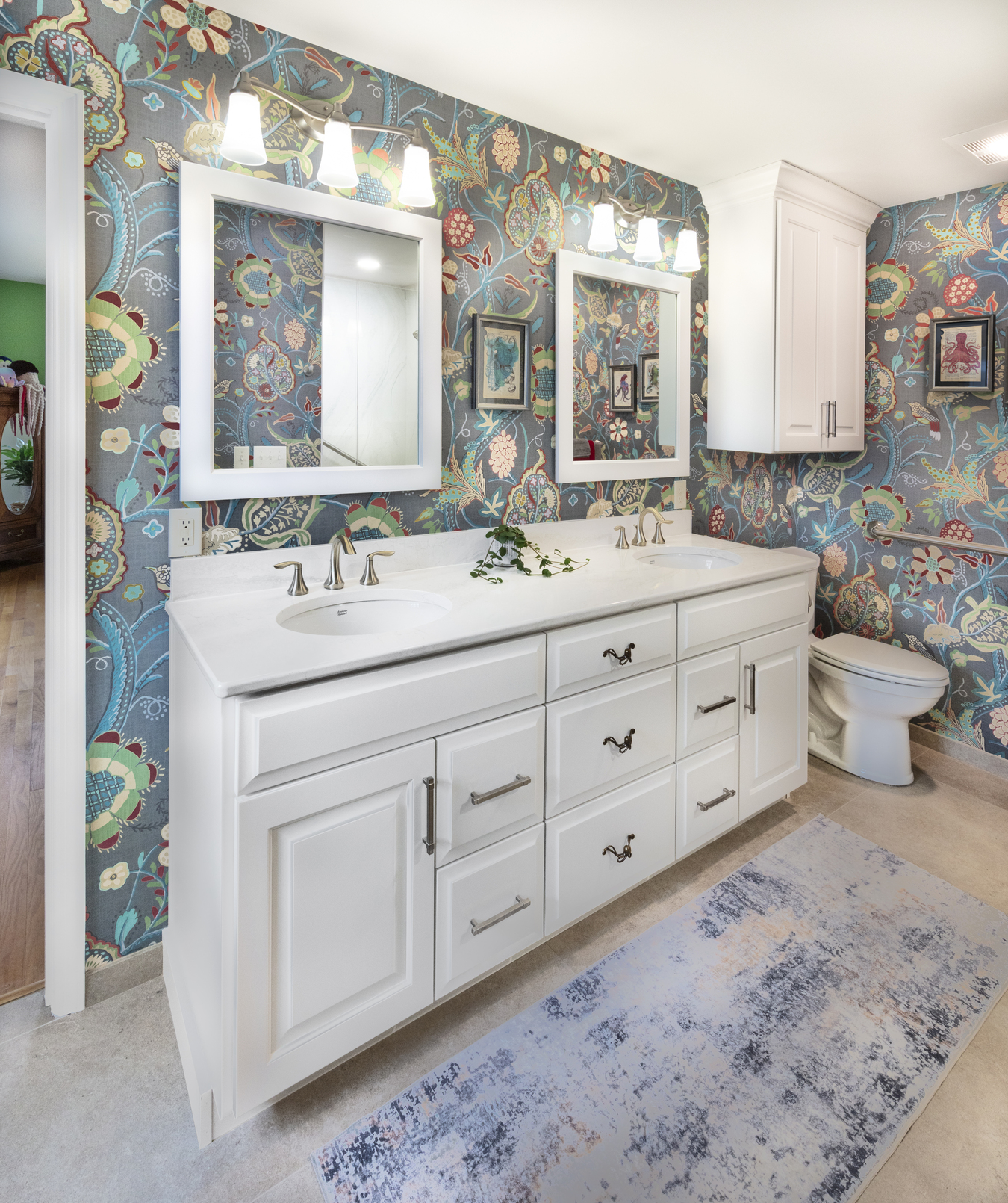 Bright bathroom with bold floral wallpaper, a white double-sink vanity, illuminated mirrors, and brushed nickel fixtures.